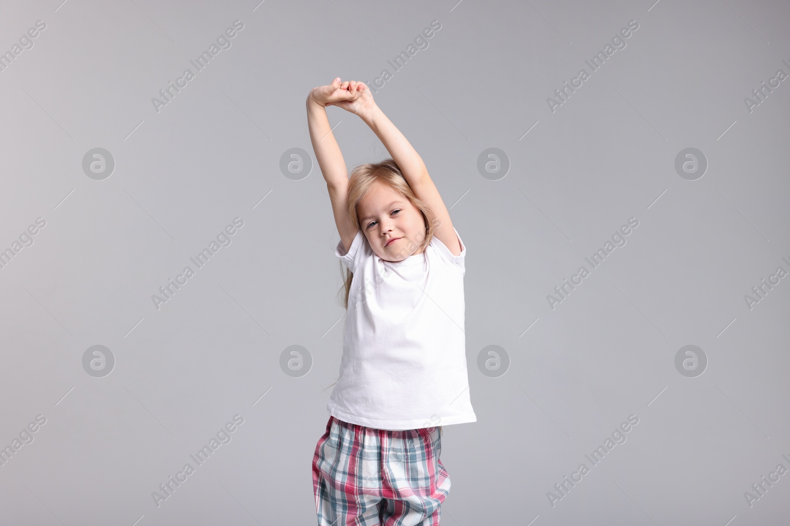 Cute little girl in pajamas stretching on grey background Photo of Cute little girl in pajamas stretching on grey background