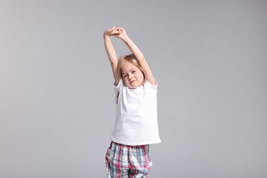 Photo of Cute little girl in pajamas stretching on grey background