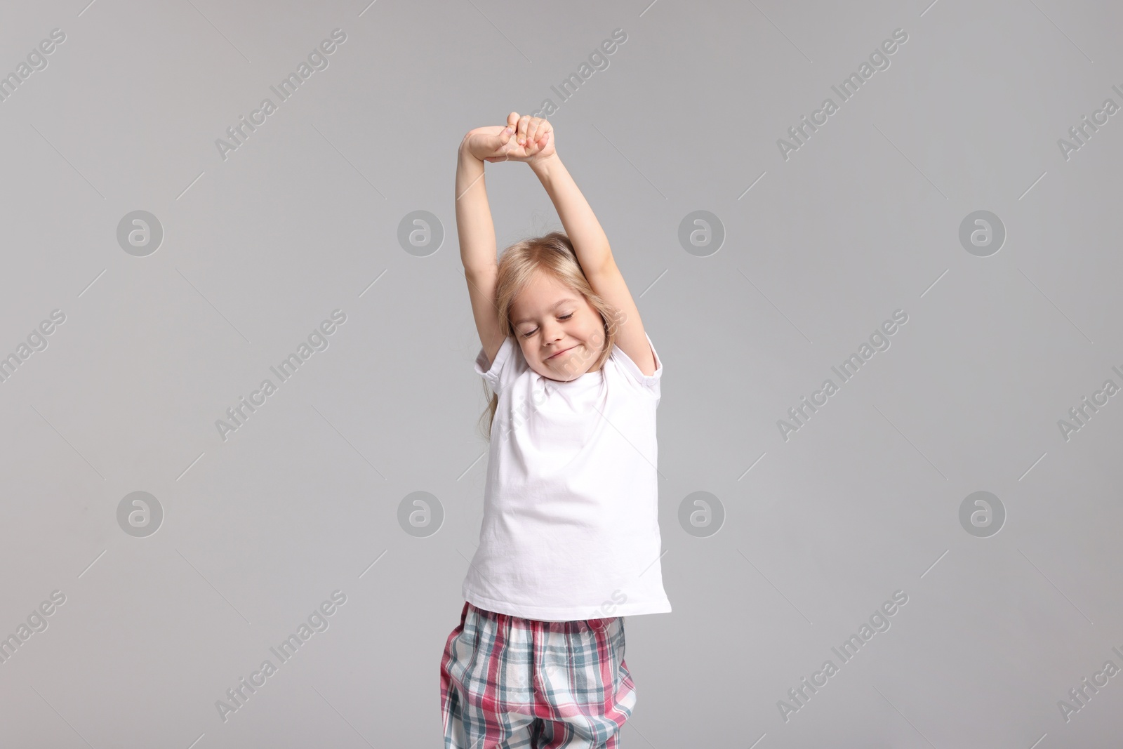 Cute little girl in pajamas stretching on grey background Photo of Cute little girl in pajamas stretching on grey background