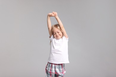 Photo of Cute little girl in pajamas stretching on grey background