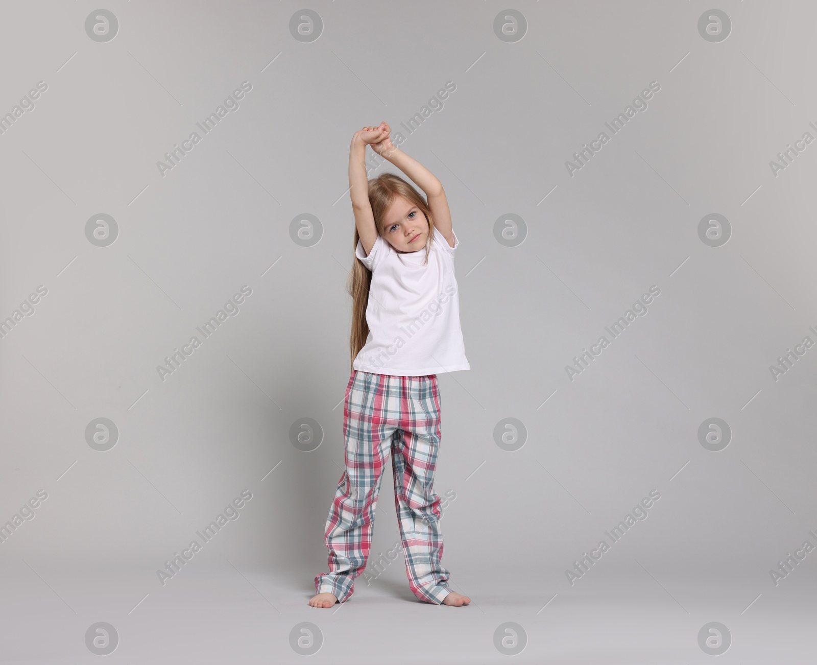 Cute little girl in pajamas stretching on grey background Photo of Cute little girl in pajamas stretching on grey background