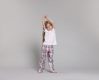Photo of Cute little girl in pajamas stretching on grey background