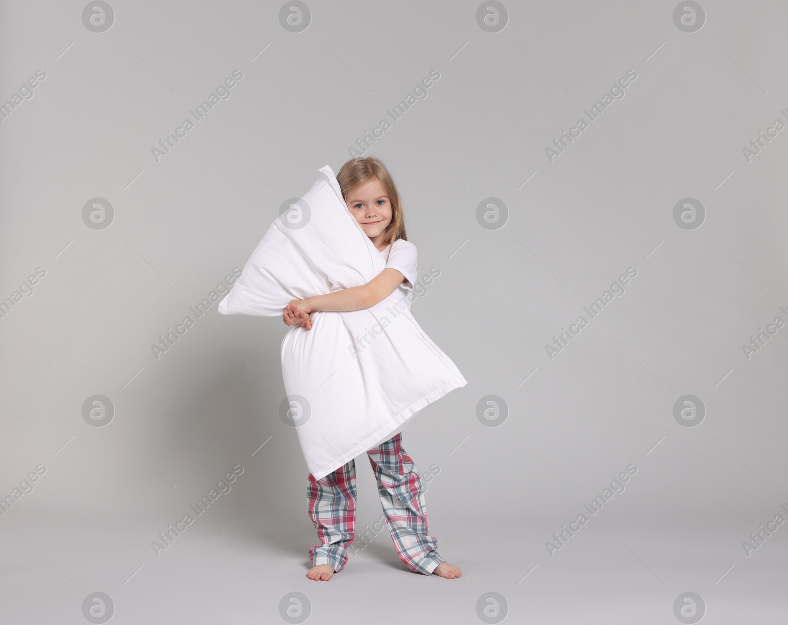 Cute little girl in pajamas with pillow on grey background Photo of Cute little girl in pajamas with pillow on grey background