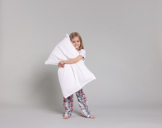 Photo of Cute little girl in pajamas with pillow on grey background