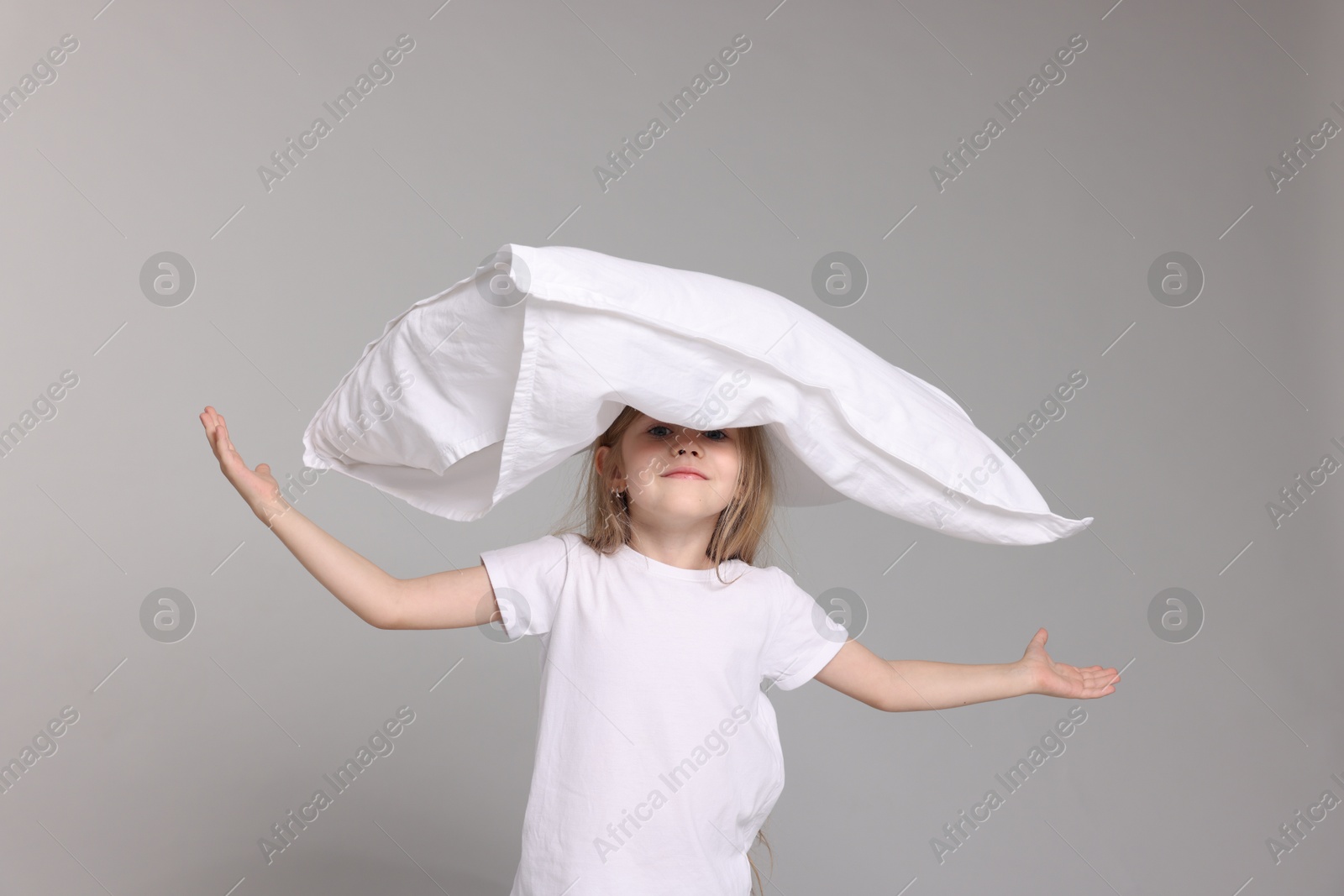 Cute little girl in pajamas with pillow on grey background Photo of Cute little girl in pajamas with pillow on grey background