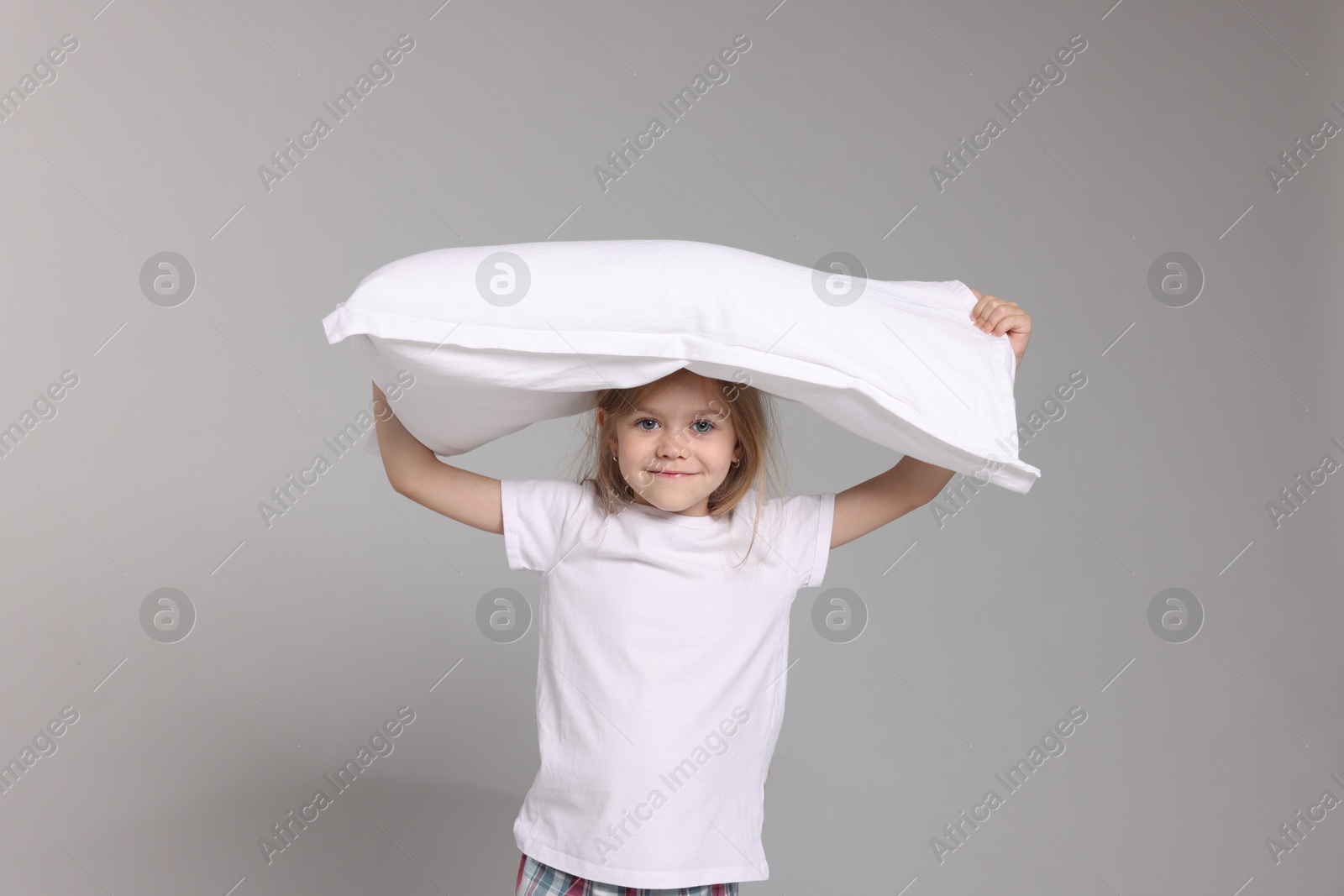 Cute little girl in pajamas with pillow on grey background Photo of Cute little girl in pajamas with pillow on grey background