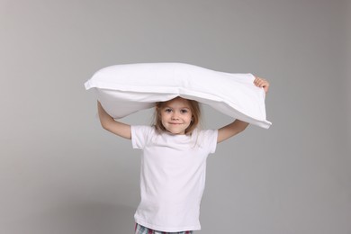 Photo of Cute little girl in pajamas with pillow on grey background