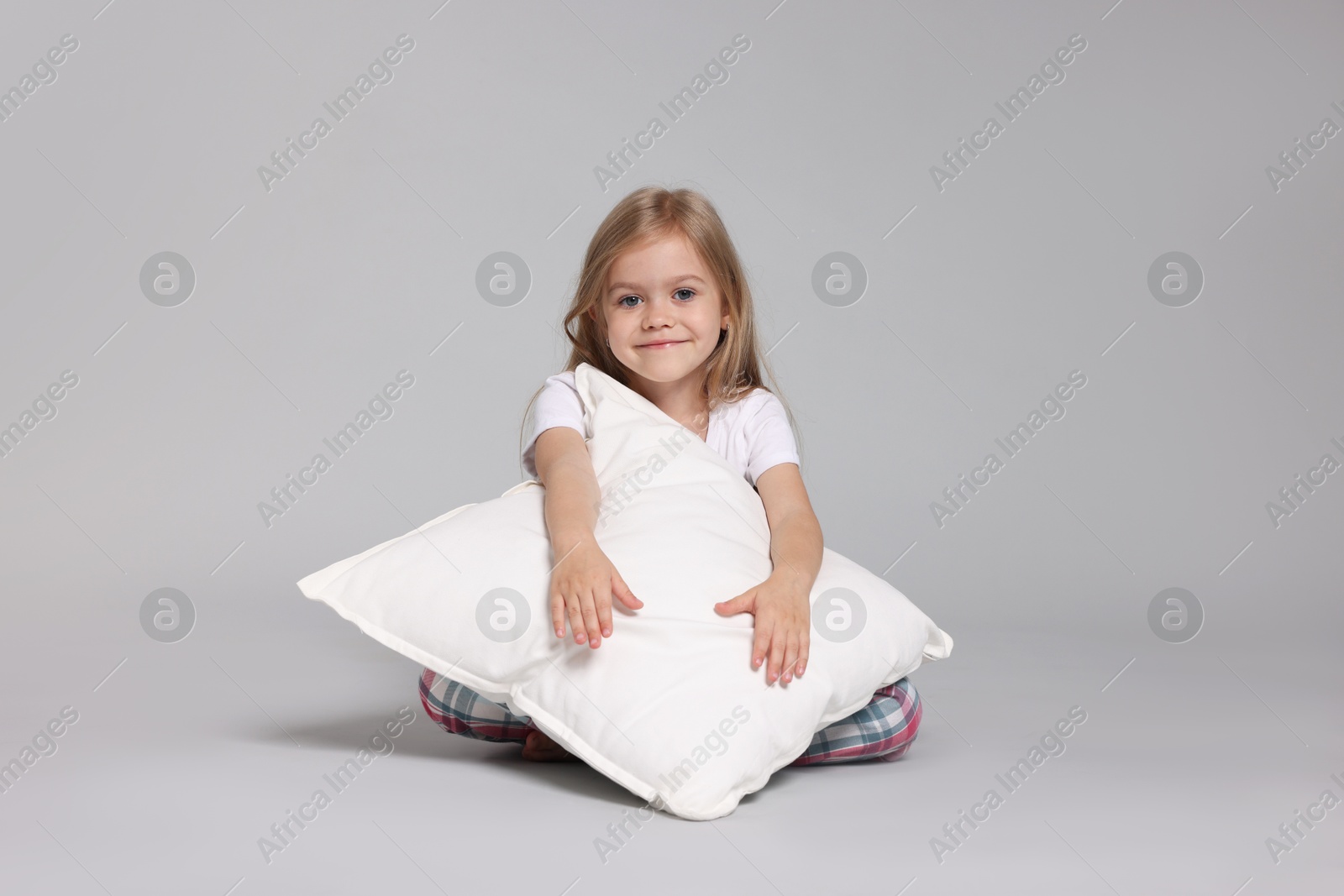 Cute little girl in pajamas with pillow on grey background Photo of Cute little girl in pajamas with pillow on grey background