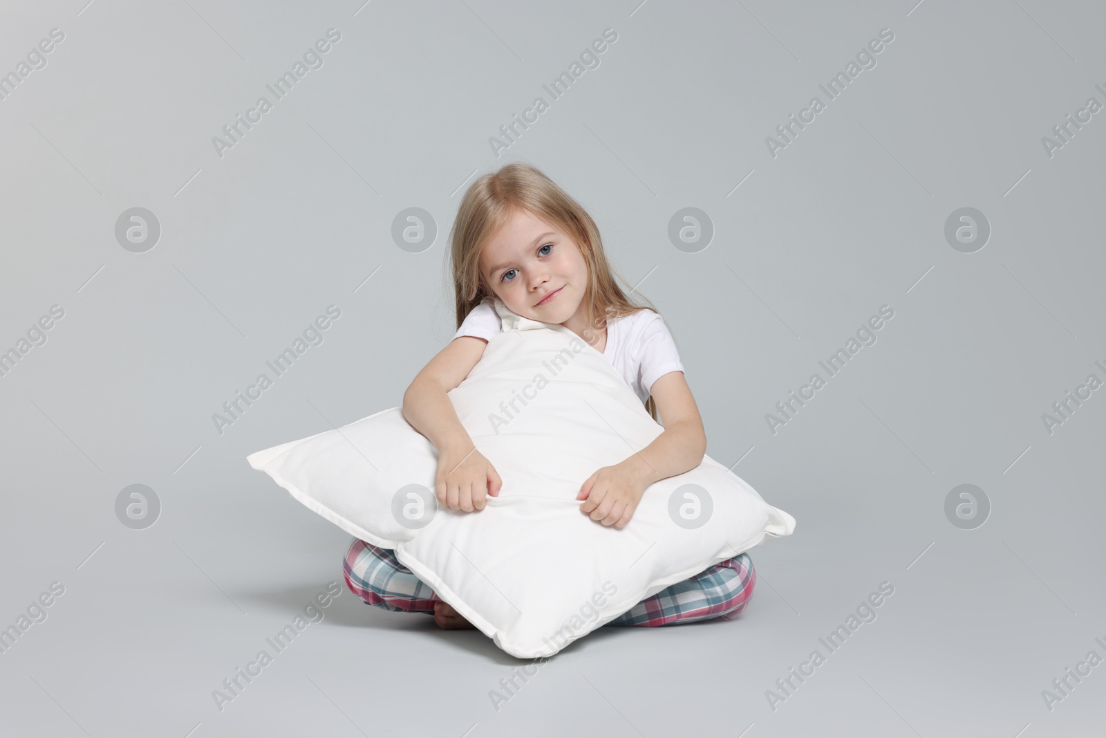 Cute little girl in pajamas with pillow on grey background Photo of Cute little girl in pajamas with pillow on grey background