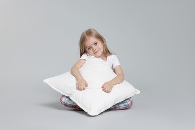 Photo of Cute little girl in pajamas with pillow on grey background