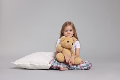 Photo of Cute little girl in pajamas with teddy bear and pillow on grey background