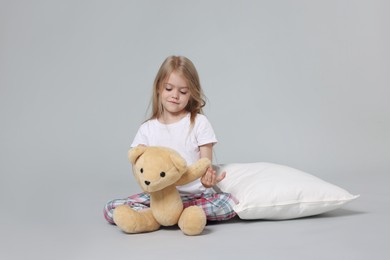 Photo of Cute little girl in pajamas with teddy bear and pillow on grey background