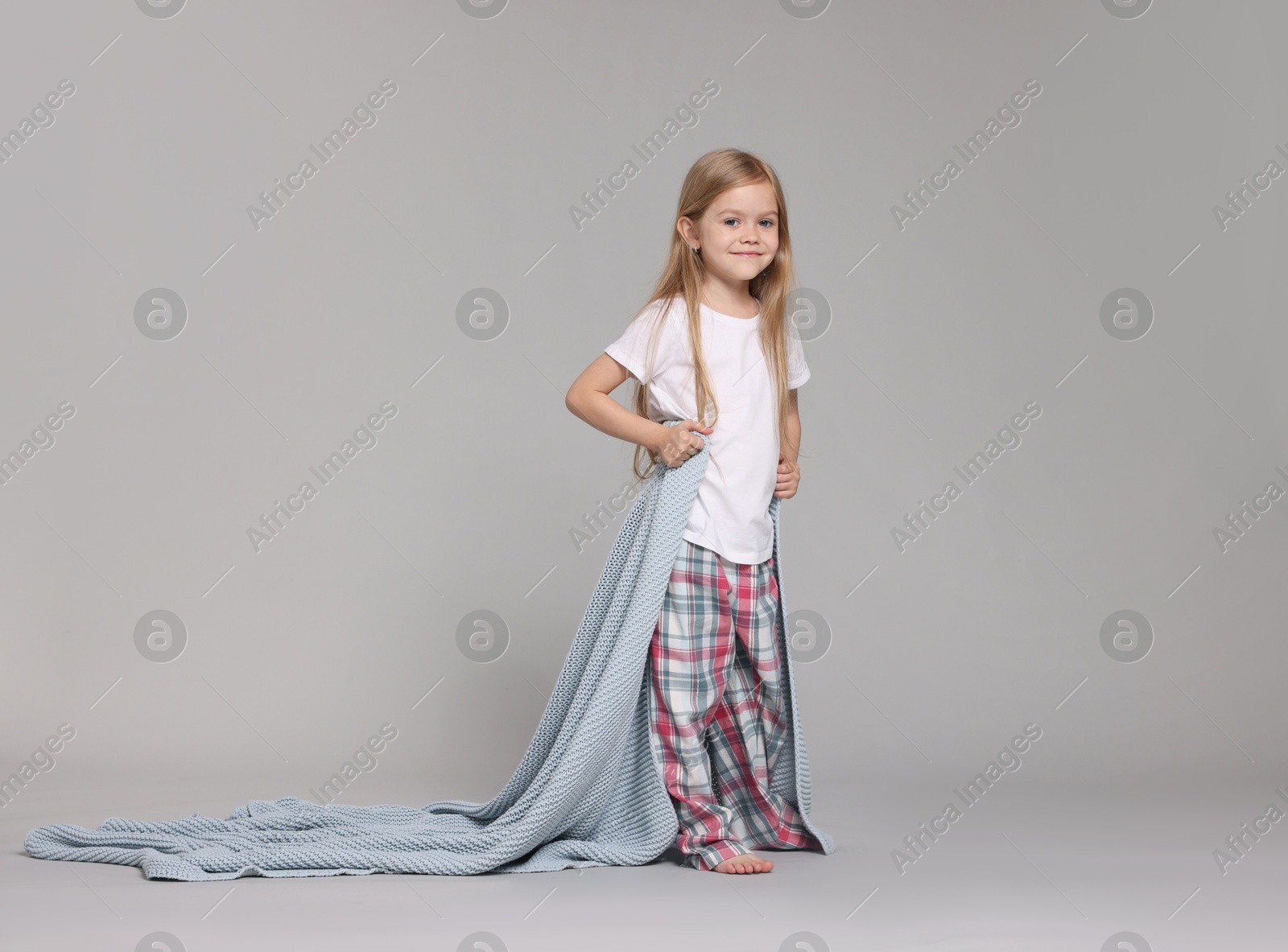 Photo of Cute little girl in pajamas with plaid on grey background