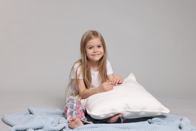 Photo of Cute little girl in pajamas with pillow and plaid on grey background