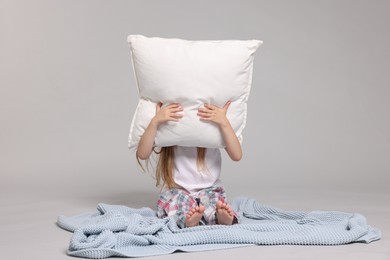 Photo of Cute little girl in pajamas with pillow and plaid on grey background
