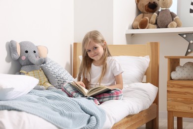 Photo of Little girl reading book in bed at home