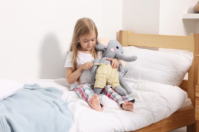 Photo of Little girl with toy elephant in bed at home