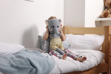 Photo of Little girl with toy elephant in bed at home