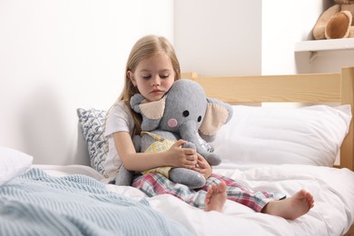 Photo of Little girl with toy elephant in bed at home
