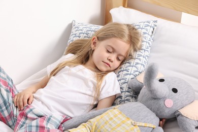 Photo of Little girl sleeping with toy elephant in bed at home