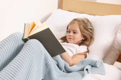 Photo of Little girl reading book in bed at home