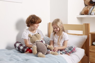 Photo of Cute children with teddy bear on bed at home