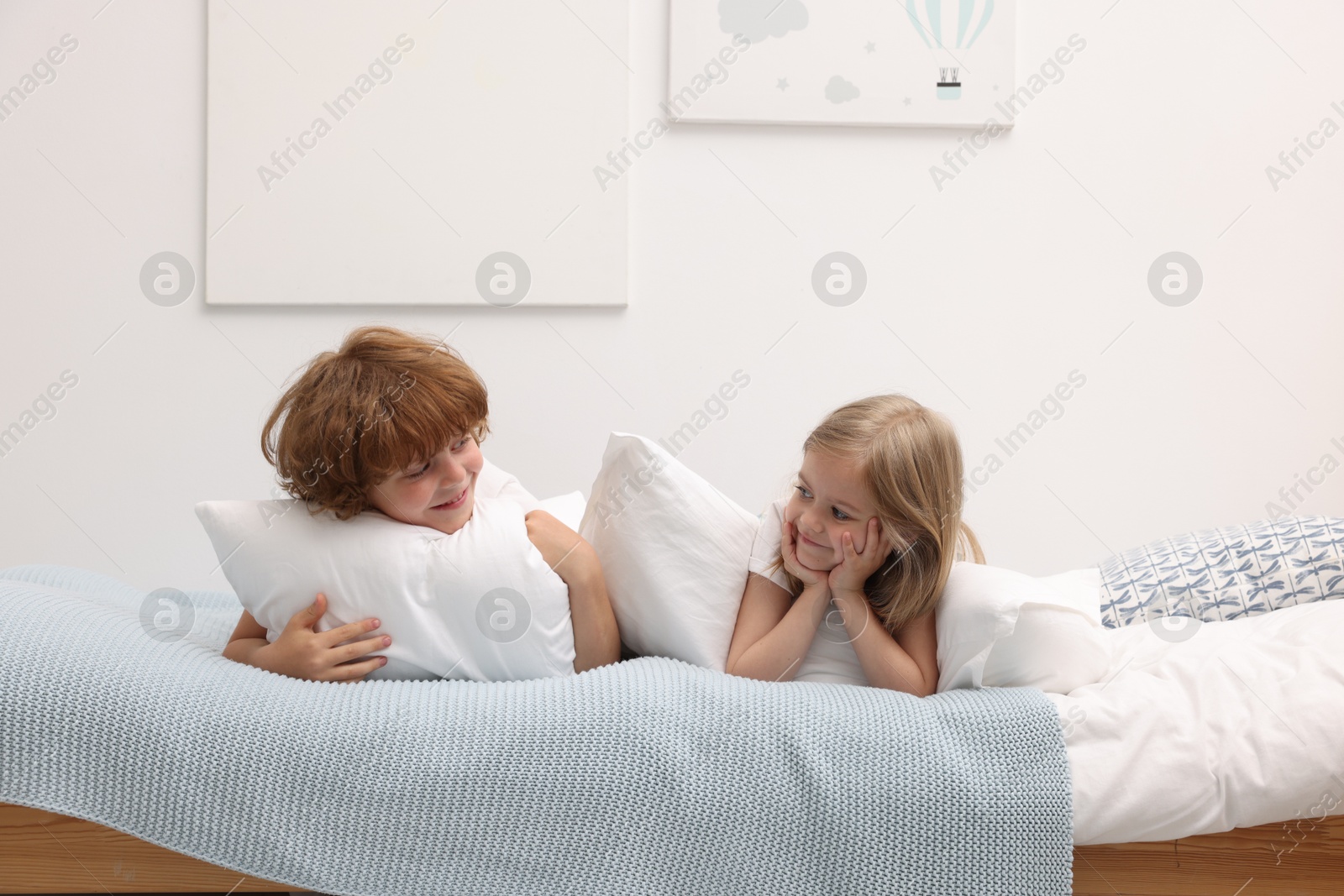 Cute children with pillows lying on bed at home Photo of Cute children with pillows lying on bed at home
