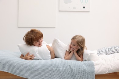 Photo of Cute children with pillows lying on bed at home