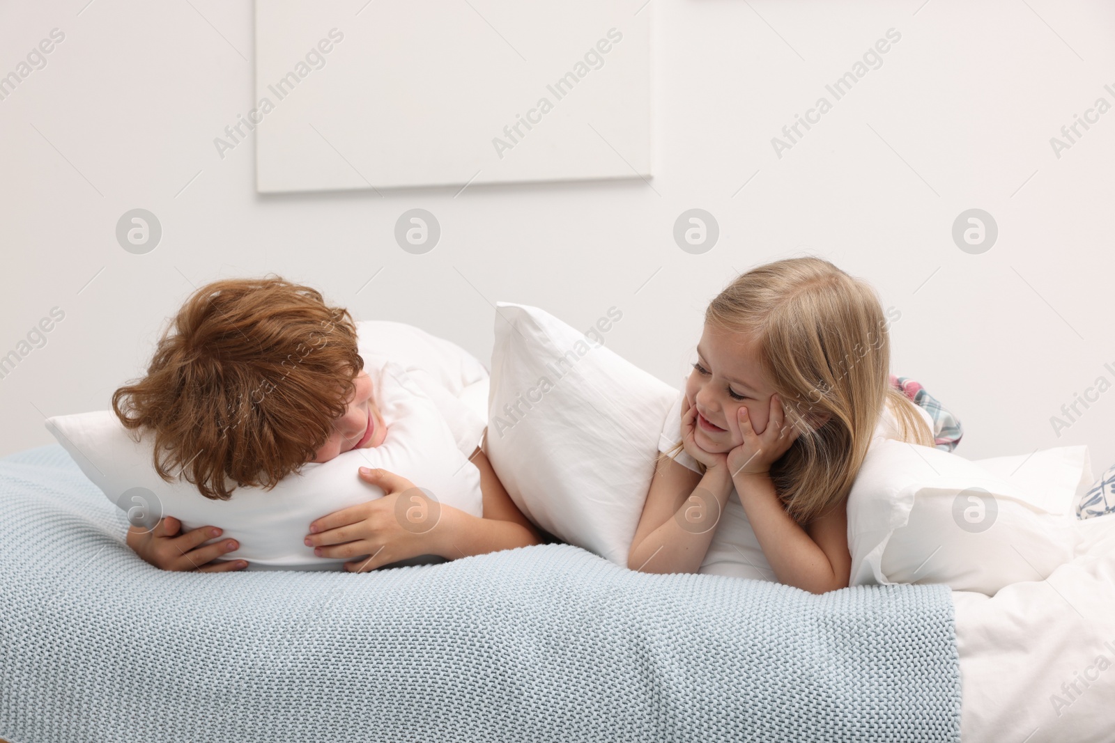 Cute children with pillows lying on bed at home Photo of Cute children with pillows lying on bed at home
