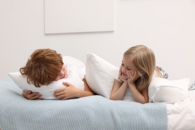 Photo of Cute children with pillows lying on bed at home