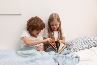 Photo of Cute children reading book on bed at home
