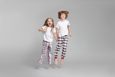 Photo of Cute little children in pajamas jumping on grey background