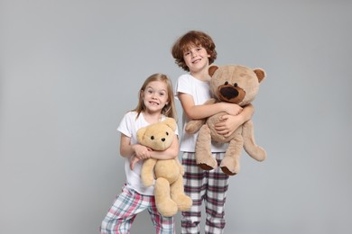 Photo of Cute little children in pajamas with teddy bears on grey background