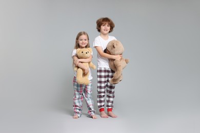Photo of Cute little children in pajamas with teddy bears on grey background