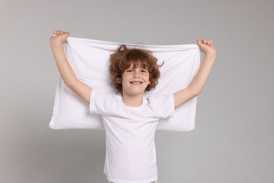 Photo of Cute little boy in pajamas with pillow on grey background