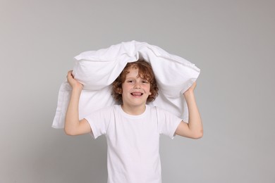Photo of Cute little boy in pajamas with pillow on grey background