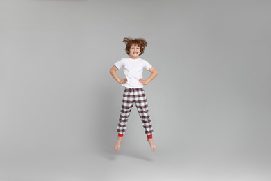 Photo of Cute little boy in pajamas jumping on grey background