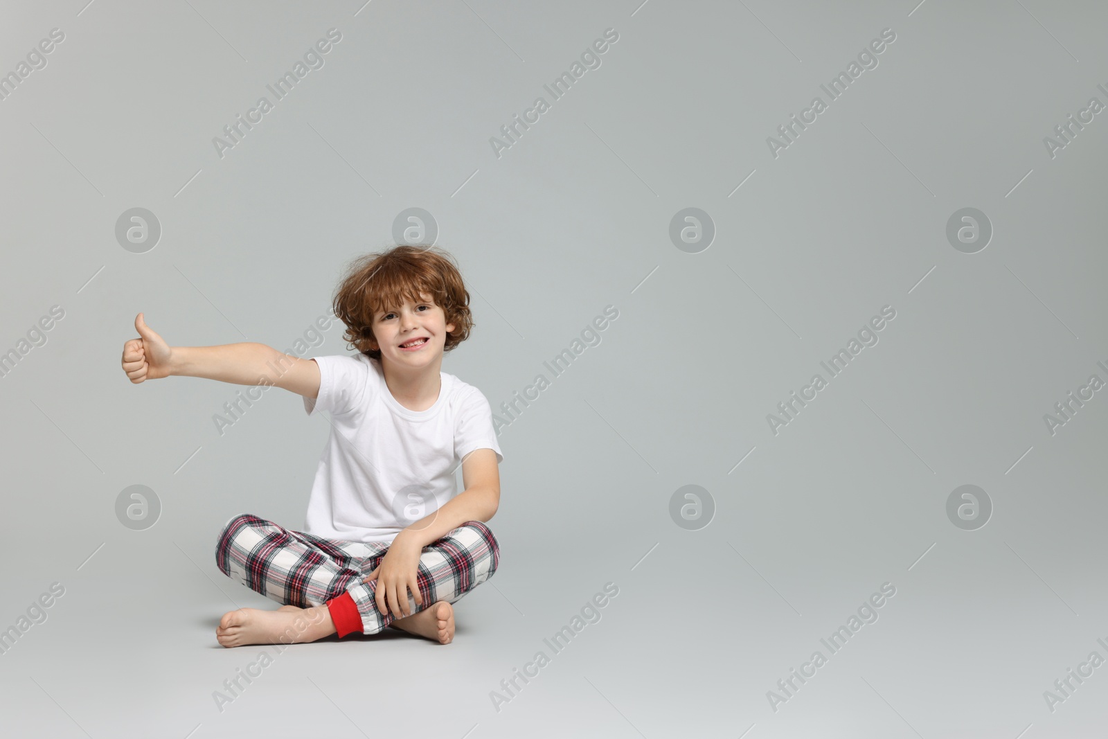 Photo of Cute little boy in pajamas showing thumbs up on grey background. Space for text