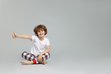 Photo of Cute little boy in pajamas showing thumbs up on grey background. Space for text