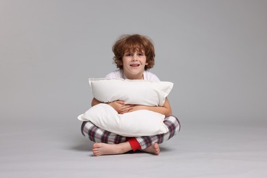Photo of Cute little boy in pajamas with pillow on grey background