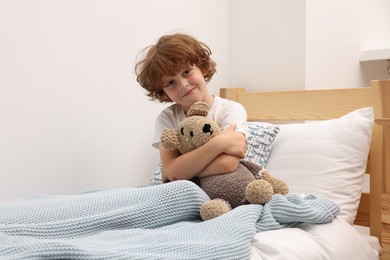 Photo of Little boy with teddy bear in bed at home