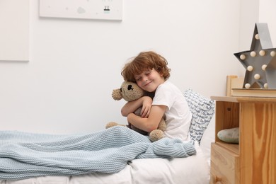 Photo of Little boy with teddy bear in bed at home