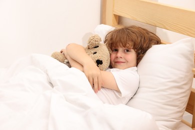 Photo of Little boy with teddy bear in bed at home