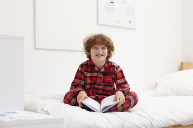 Photo of Little boy with book on bed at home