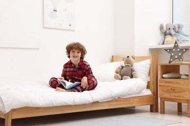Photo of Little boy with book on bed at home