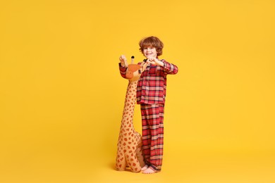 Photo of Cute little boy in pajamas with toy giraffe on yellow background