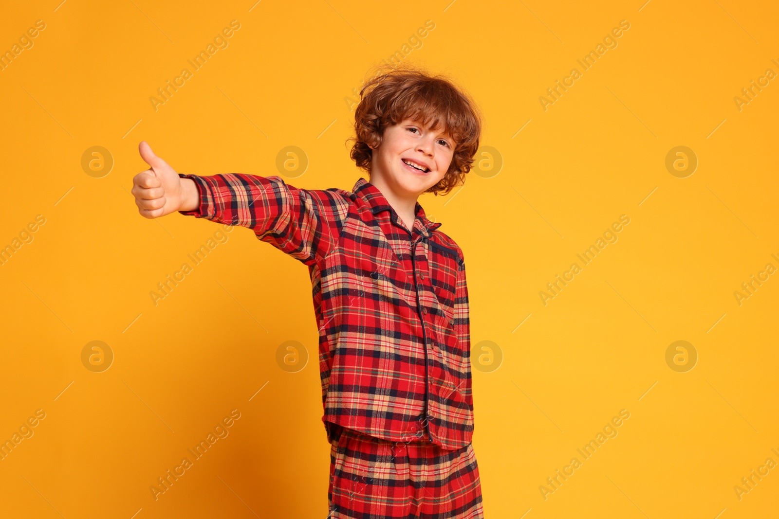 Photo of Cute little boy in pajamas showing thumbs up on yellow background
