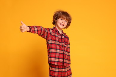 Photo of Cute little boy in pajamas showing thumbs up on yellow background