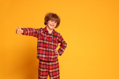 Photo of Cute little boy in pajamas showing thumbs up on yellow background. Space for text