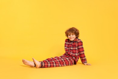 Photo of Cute little boy in pajamas on yellow background. Space for text